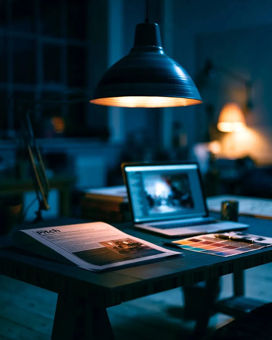 A printed pitch document and laptop on a studio desk at night